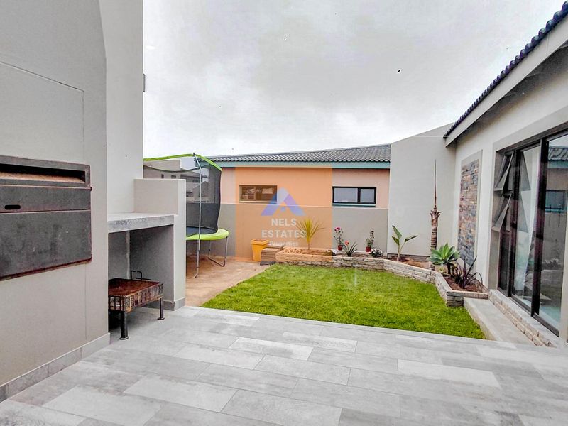 Covered patio area featuring a built-in braai, tiled flooring, and direct access to a small landscaped garden with a stone-clad feature wall.