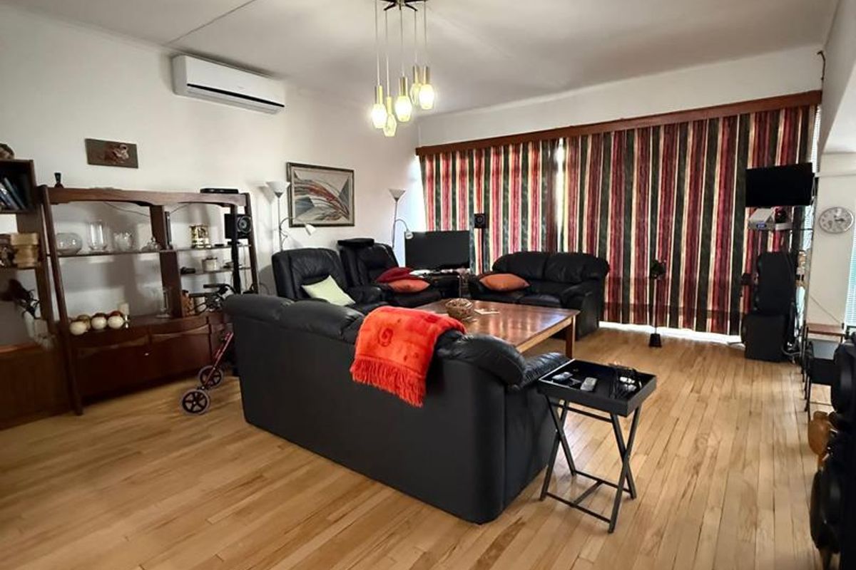Spacious living room featuring light-toned hardwood flooring, a wall-mounted air conditioning unit, and large floor-to-ceiling window treatments.