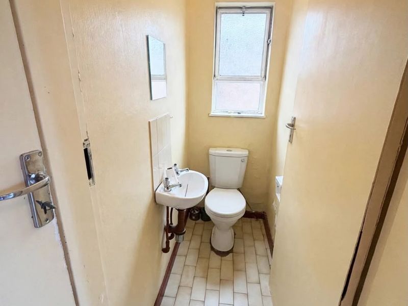A compact, dated bathroom featuring a toilet, wall-mounted basin, and tiled flooring, requiring cosmetic updates to improve its overall condition and appeal.