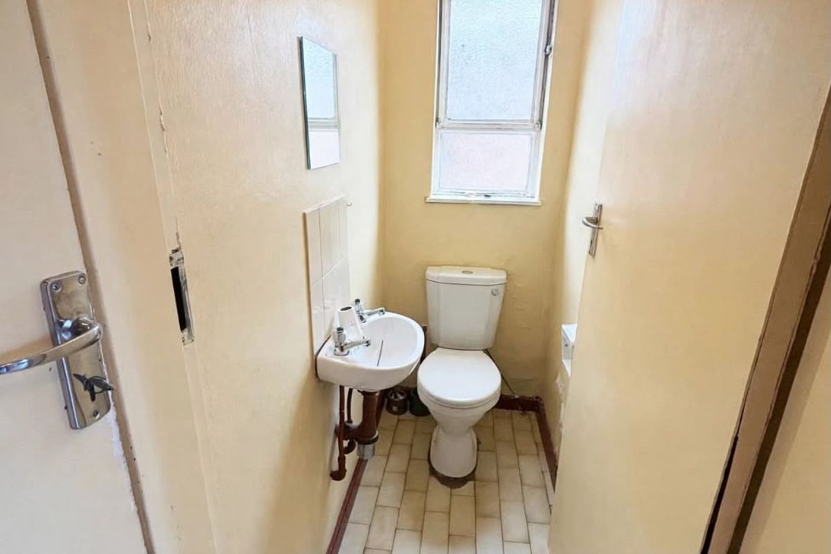 A compact, dated bathroom featuring a toilet, wall-mounted basin, and tiled flooring, requiring cosmetic updates to improve its overall condition and appeal.