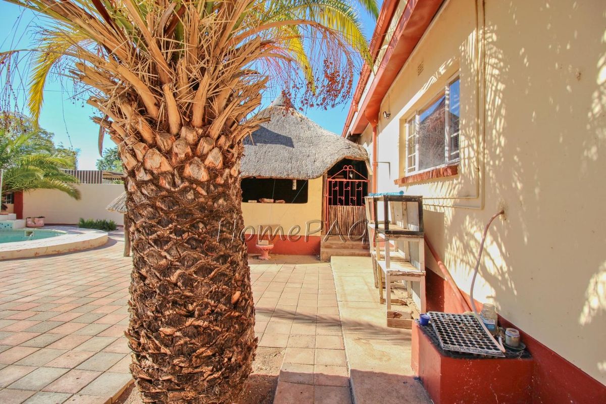 Rear exterior view featuring a paved patio area, swimming pool, and a traditional thatched lapa structure.