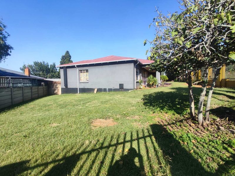 Rear view of the property featuring a spacious lawn, precast boundary wall, and a painted masonry exterior with a corrugated metal roof.