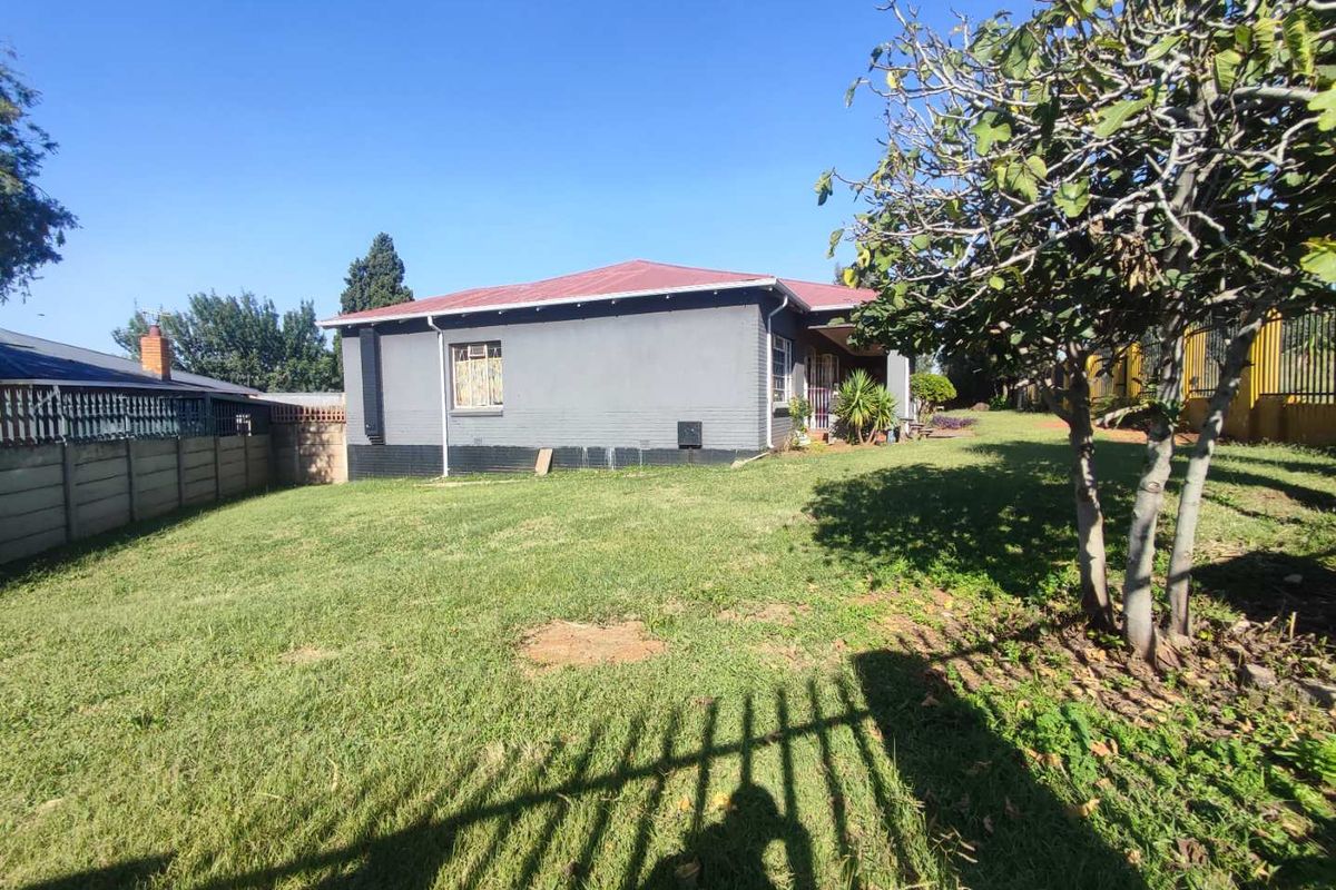 Rear view of the property featuring a spacious lawn, precast boundary wall, and a painted masonry exterior with a corrugated metal roof.