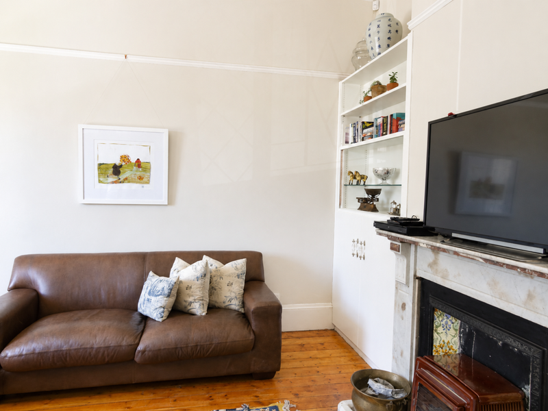 A cozy living room featuring original timber flooring, a classic fireplace with built-in shelving, and traditional picture rails.