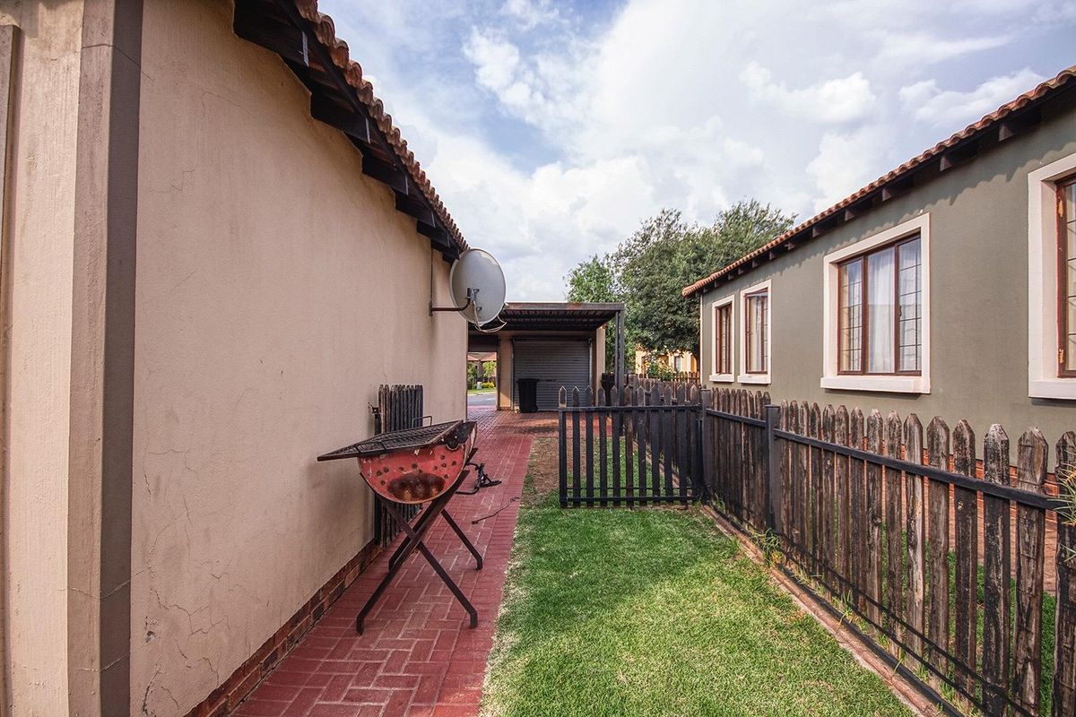 A side exterior view showing a paved walkway, timber fencing, and a carport structure with a tiled roof.