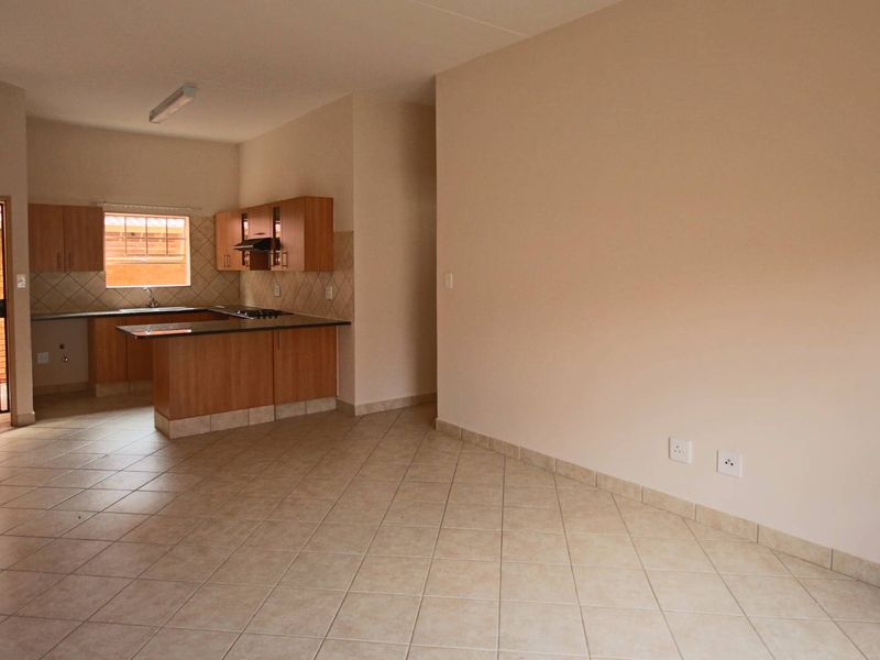 An open-plan living and kitchen area featuring tiled flooring, wooden cabinetry, and a built-in hob, offering a functional and versatile living space.