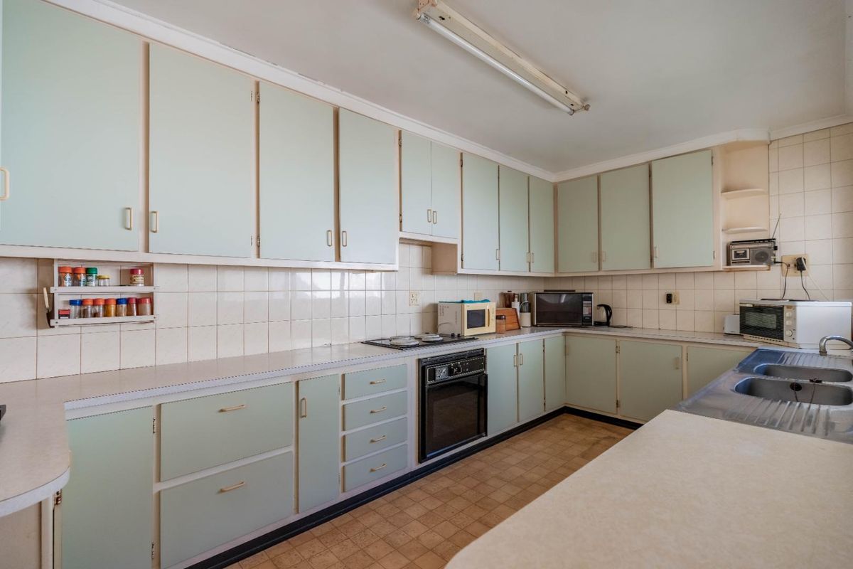 A dated kitchen featuring original cabinetry, laminate countertops, a built-in oven, and a double-bowl stainless steel sink with a tiled backsplash.