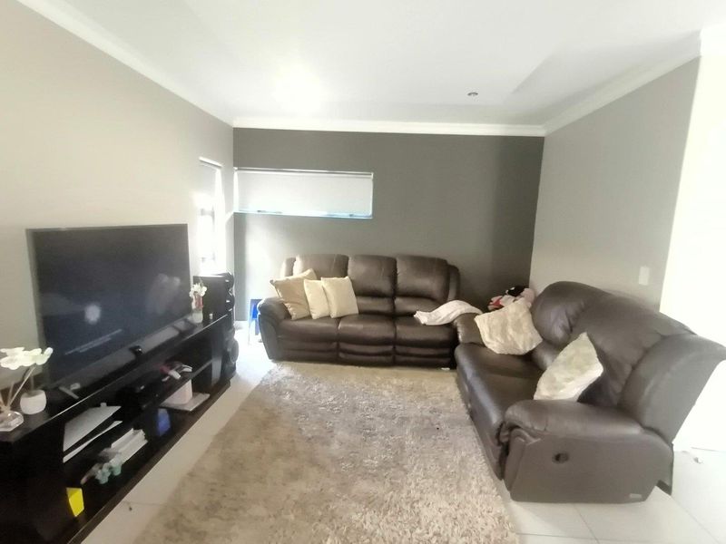 A comfortable living room featuring tiled flooring, recessed downlighting, and a neutral color palette with a dark accent wall.