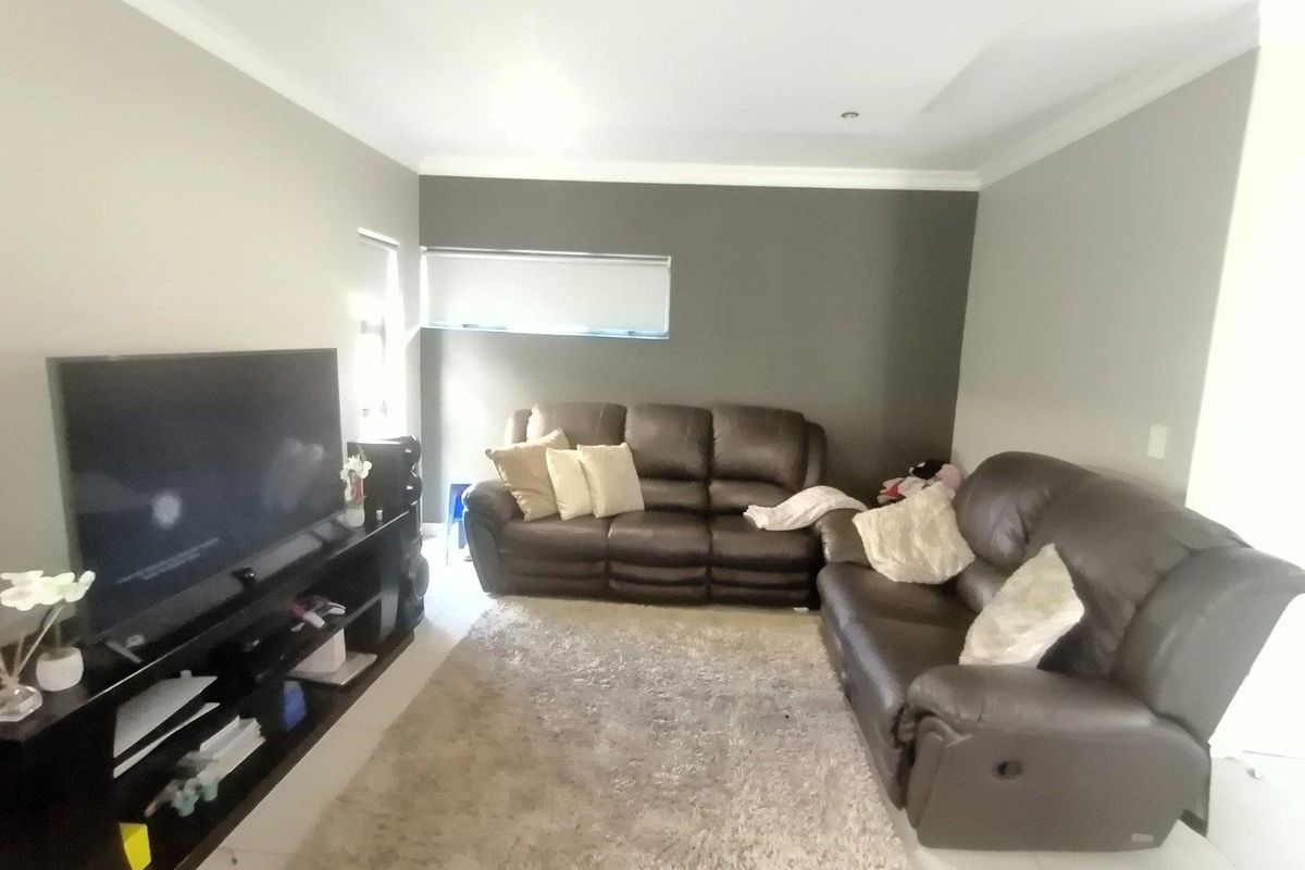 A comfortable living room featuring tiled flooring, recessed downlighting, and a neutral color palette with a dark accent wall.