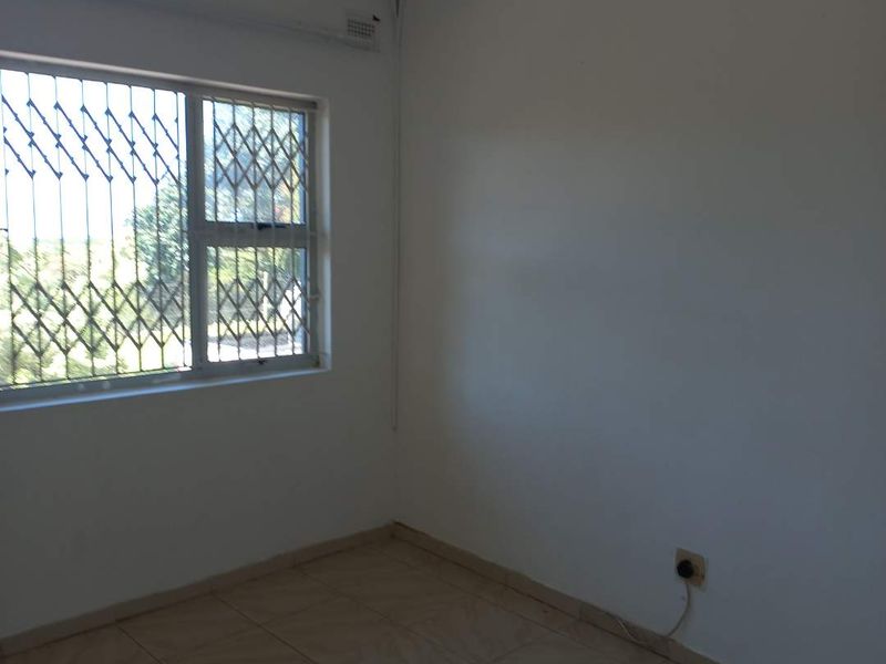 A simple, empty bedroom featuring tiled flooring and a window fitted with security bars.