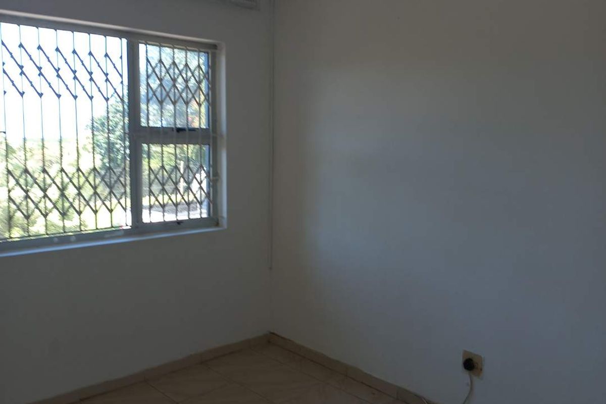 A simple, empty bedroom featuring tiled flooring and a window fitted with security bars.