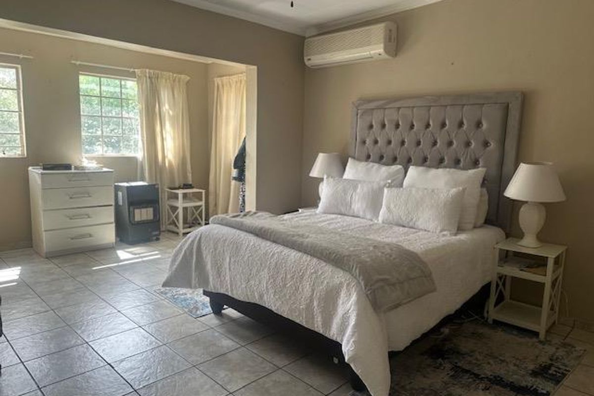 Spacious bedroom featuring tiled flooring, a wall-mounted air conditioning unit, and large windows allowing for natural light.