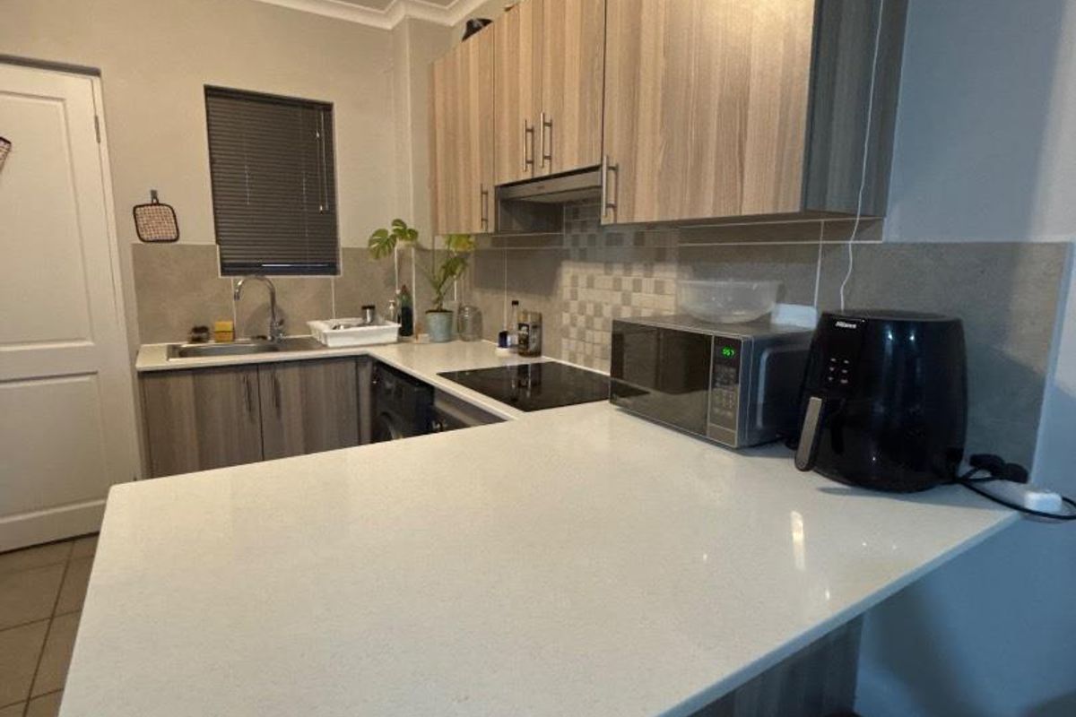 A functional kitchen featuring modern wood-look cabinetry, stone countertops, a tiled backsplash, and integrated cooking appliances.