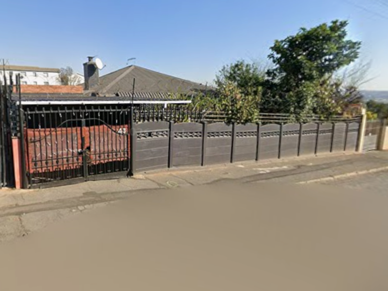Front exterior view of the property featuring a secure precast concrete boundary wall, wrought iron gate, and tiled roof structure.