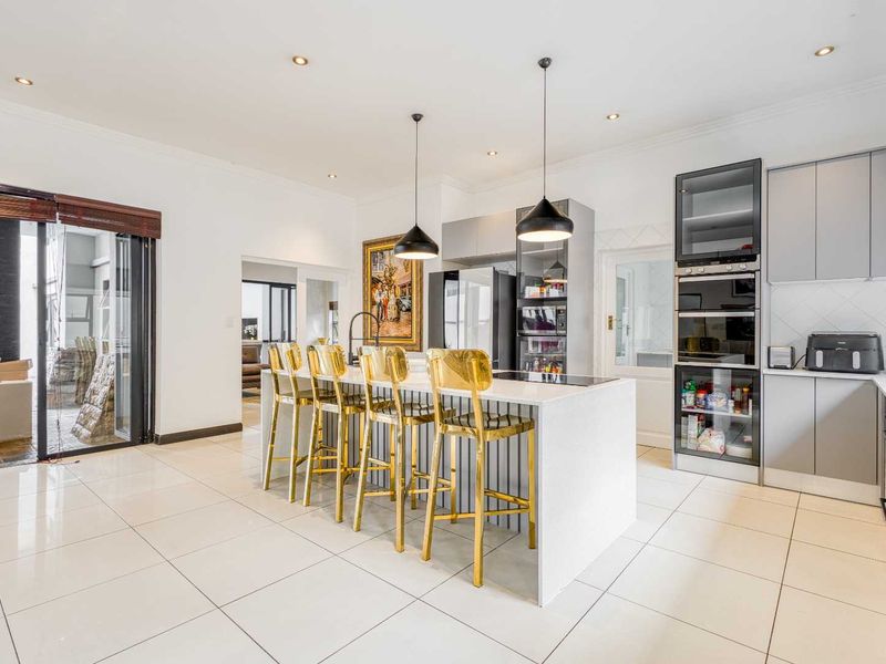 Modern kitchen featuring a central island with quartz countertops, built-in appliances, sleek cabinetry, and large format floor tiles, opening to an outdoor patio area.