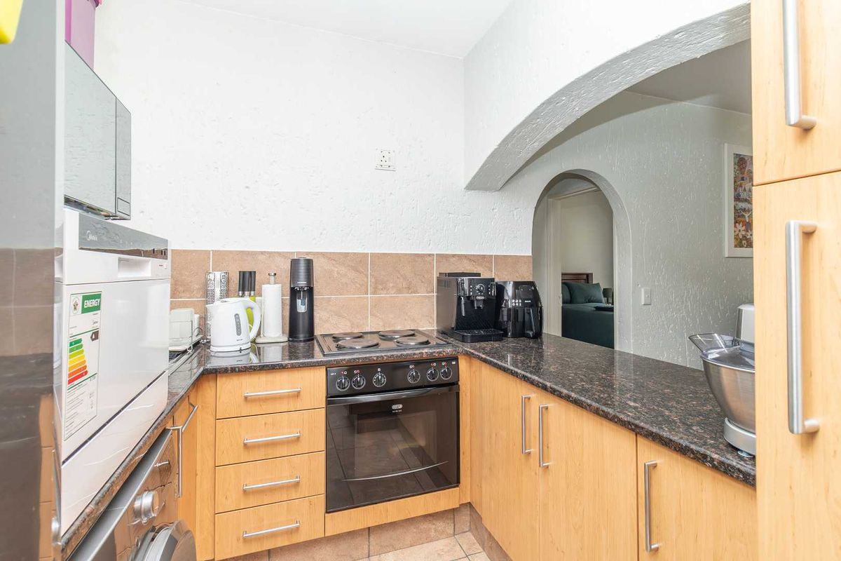 Compact kitchen featuring light wood cabinetry, dark granite countertops, built-in oven, electric hob, and a tiled backsplash with an arched opening to the living area.