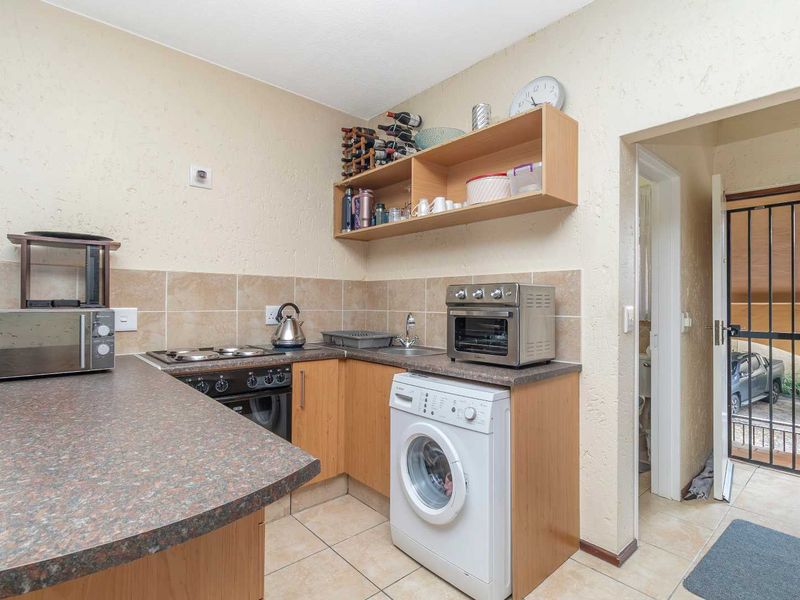 Compact kitchen featuring laminate countertops, built-in oven and hob, tiled backsplash, and integrated laundry plumbing, with direct access to an exterior security gate.
