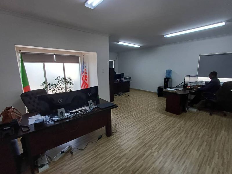 A functional office space featuring laminate flooring, recessed window alcoves with roller blinds, and overhead fluorescent lighting.