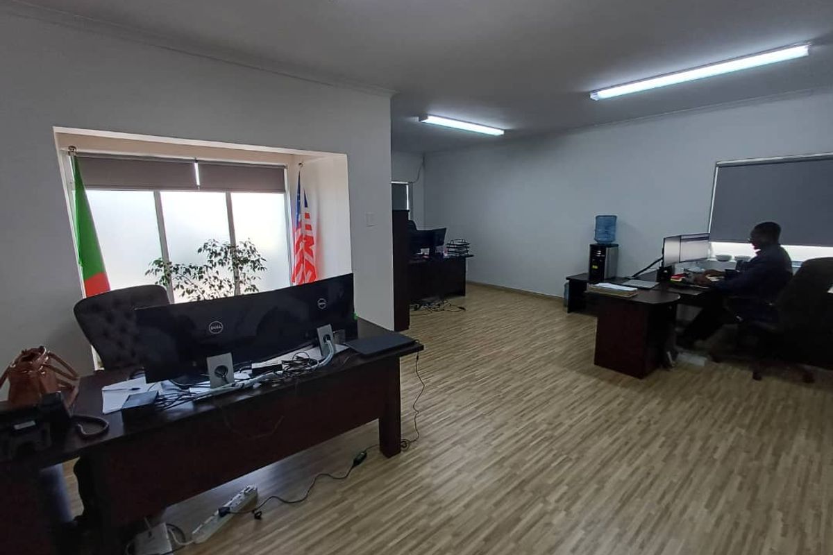 A functional office space featuring laminate flooring, recessed window alcoves with roller blinds, and overhead fluorescent lighting.