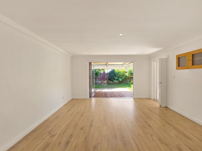 Bright and spacious living area featuring light wood-look laminate flooring, recessed lighting, and bi-fold doors opening directly onto a rear timber deck.