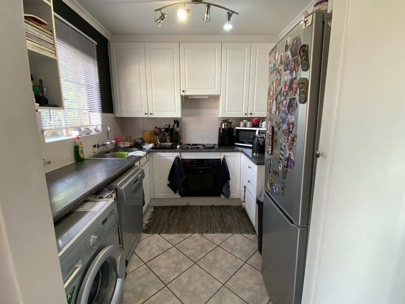 A functional galley-style kitchen featuring white cabinetry, dark laminate countertops, tiled flooring, and integrated cooking appliances.