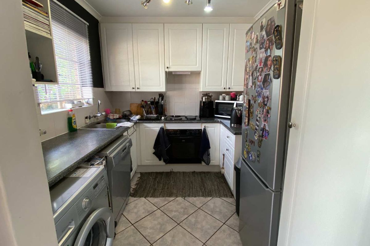 A functional galley-style kitchen featuring white cabinetry, dark laminate countertops, tiled flooring, and integrated cooking appliances.