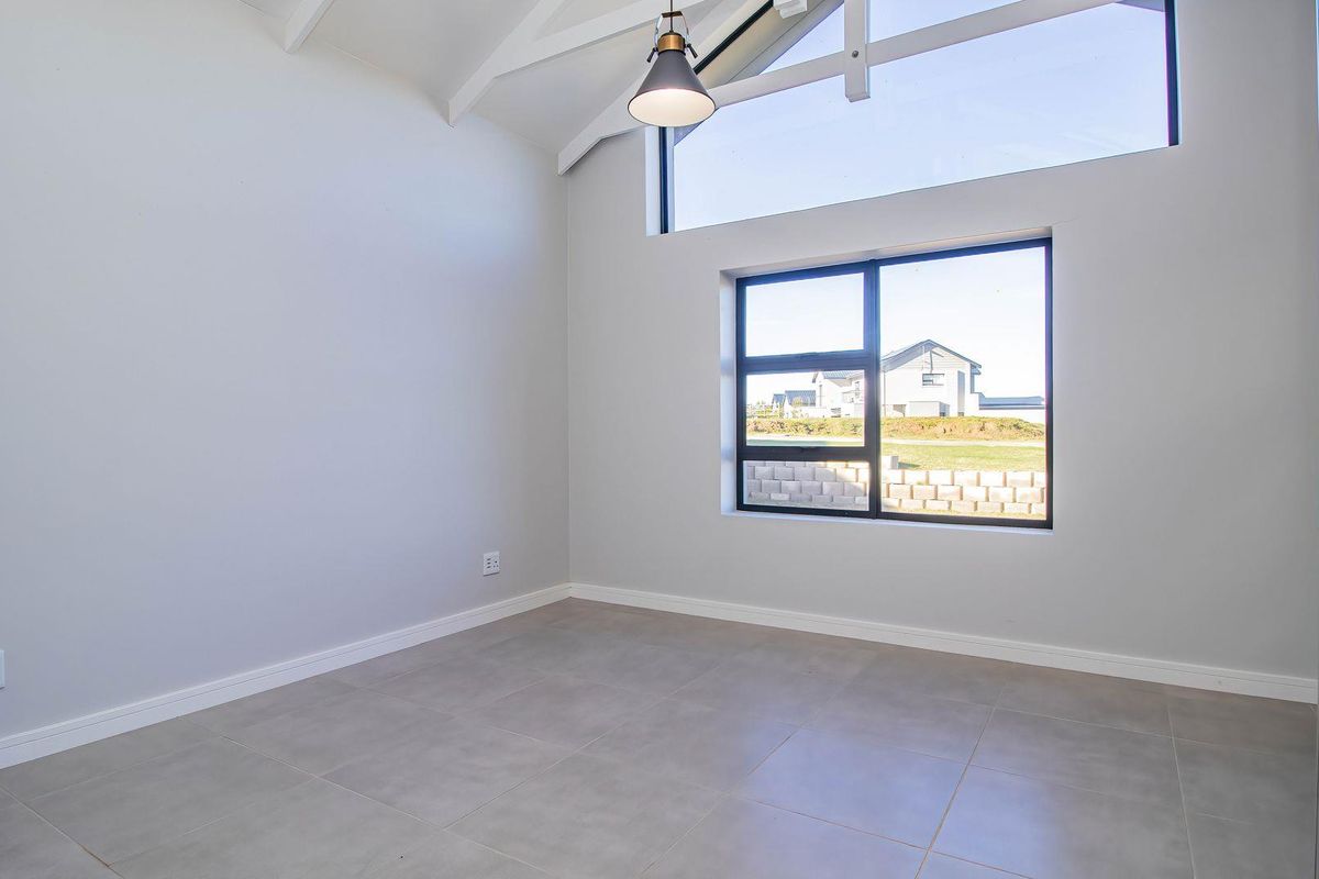 A bright, modern bedroom featuring high vaulted ceilings, large windows with natural light, tiled flooring, and built-in cabinetry.