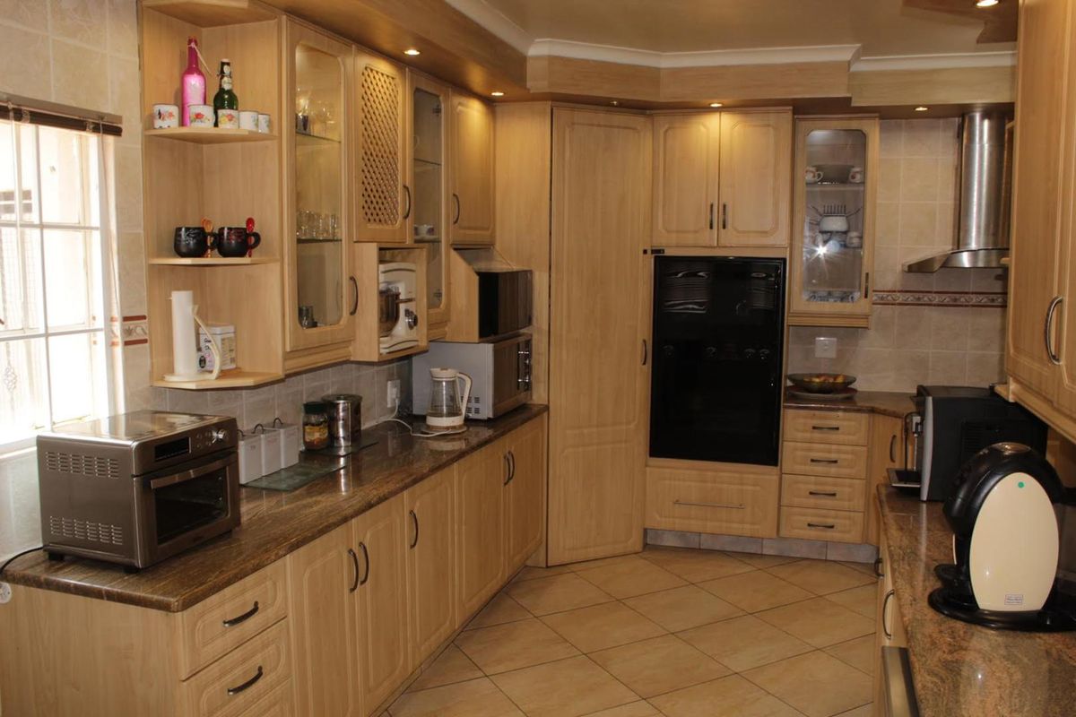 A functional kitchen featuring light wood cabinetry, granite countertops, tiled flooring, and built-in appliances including an oven and extractor fan.