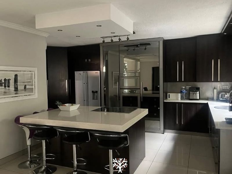 Modern kitchen featuring a central island with integrated hob, dark cabinetry, built-in appliances, and tiled flooring.
