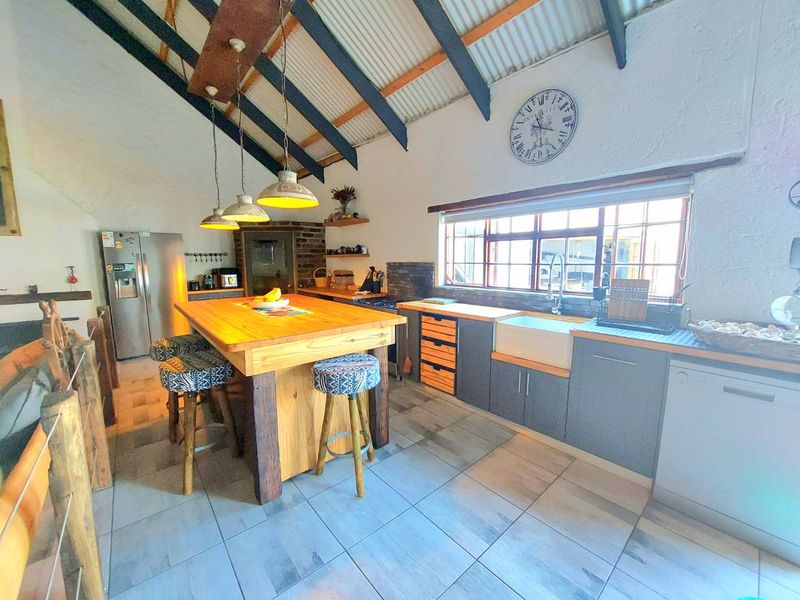 Spacious kitchen featuring exposed timber beams, a large central timber island, farmhouse sink, and modern tiled flooring with a rustic aesthetic.