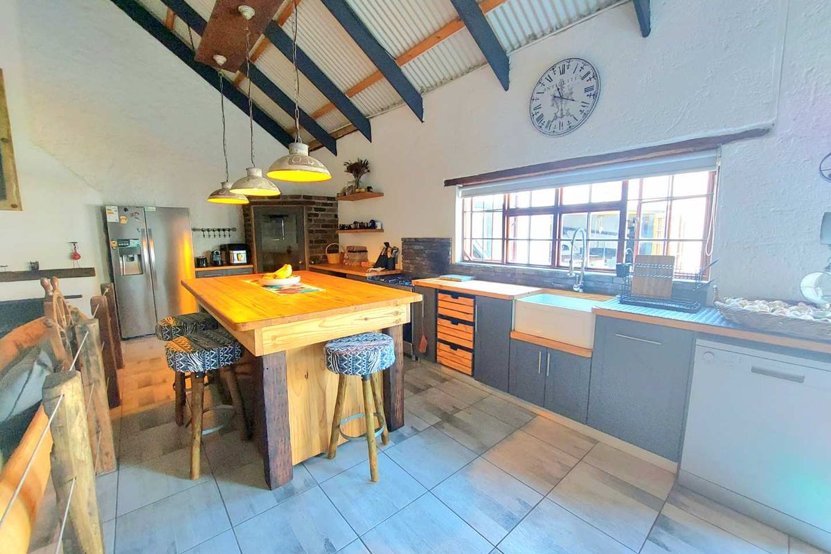 Spacious kitchen featuring exposed timber beams, a large central timber island, farmhouse sink, and modern tiled flooring with a rustic aesthetic.