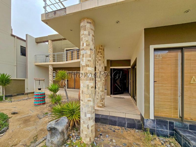 Rear exterior view featuring a covered patio with stone-clad columns, sliding glass doors, and an upper-level balcony with metal railings.