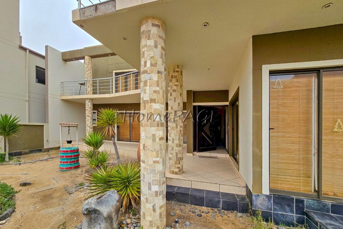 Rear exterior view featuring a covered patio with stone-clad columns, sliding glass doors, and an upper-level balcony with metal railings.
