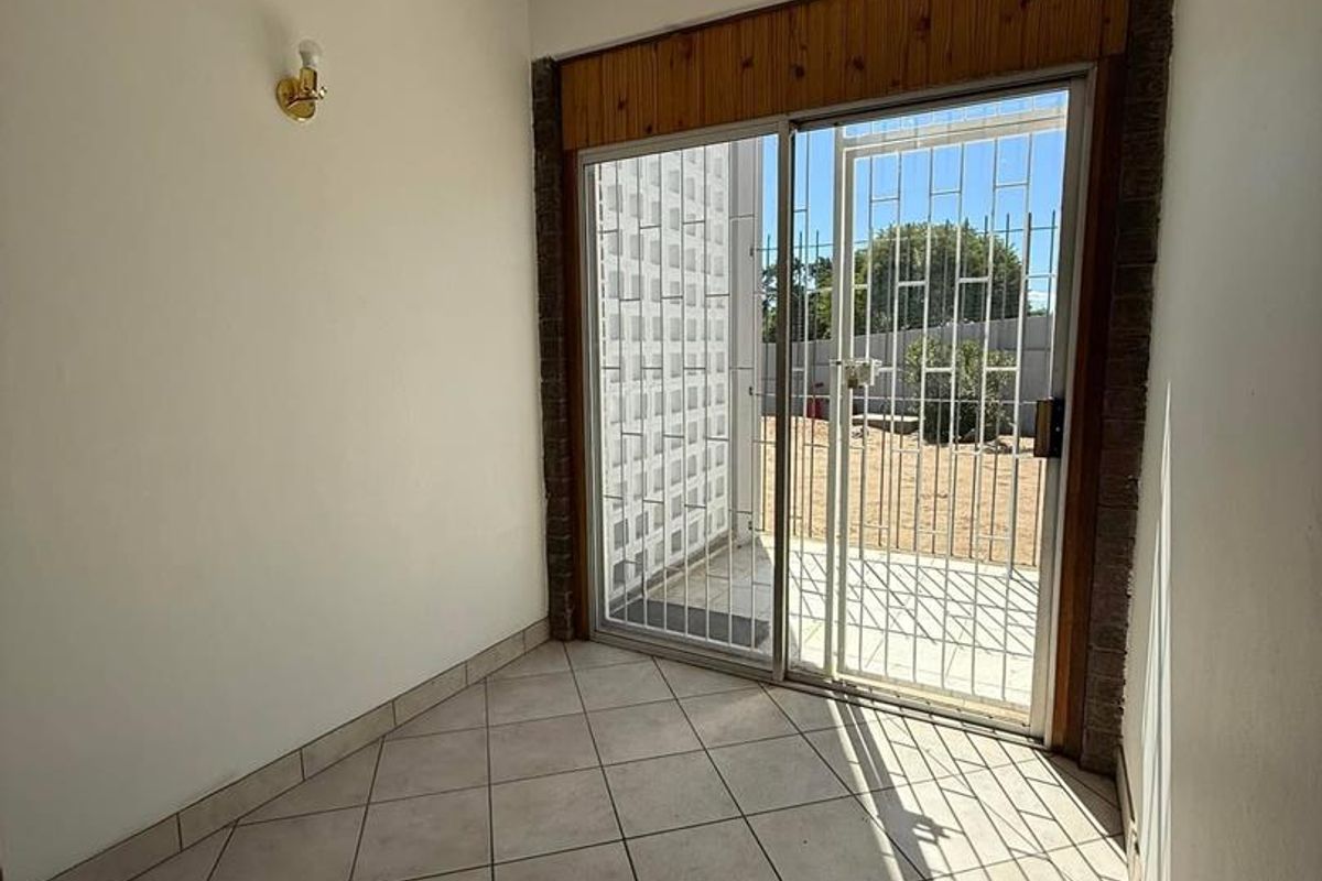 A bright, empty room featuring tiled flooring and a sliding glass door with security gate leading to an outdoor area.