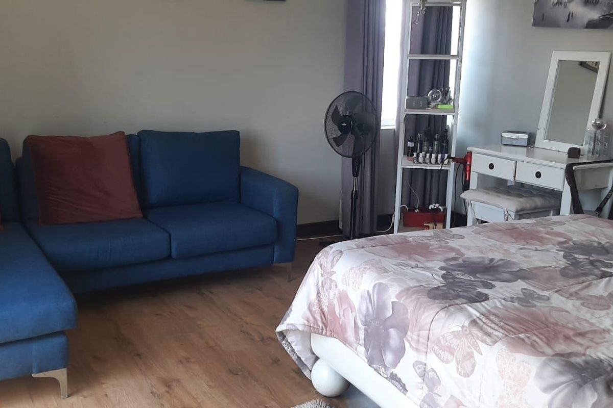 A bedroom featuring laminate flooring and neutral wall finishes, providing a functional space with room for a seating area.