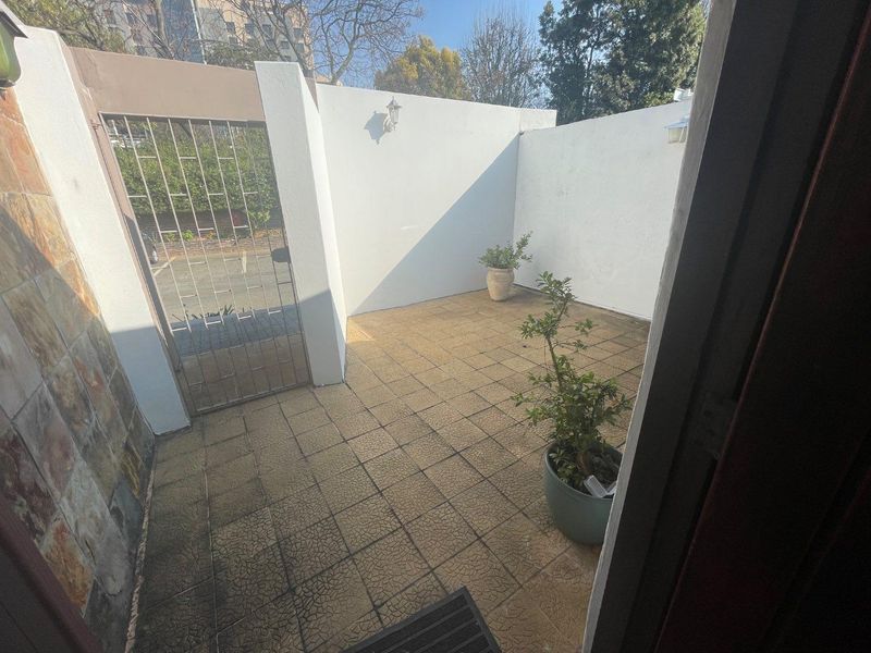 A private, enclosed paved patio area featuring a metal security gate and wall-mounted lighting, offering a secure outdoor space.
