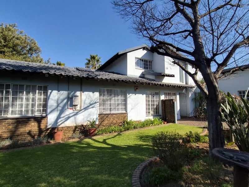 Front elevation of a residential house featuring a tiled roof, brick accents, multi-pane windows, and a well-maintained front garden with mature trees.