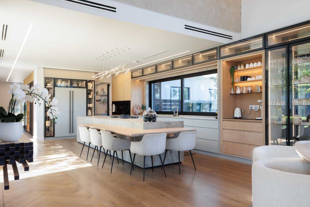 A modern, high-end kitchen featuring a large stone island, integrated cabinetry, premium timber flooring, and sophisticated recessed lighting throughout the open-plan space.