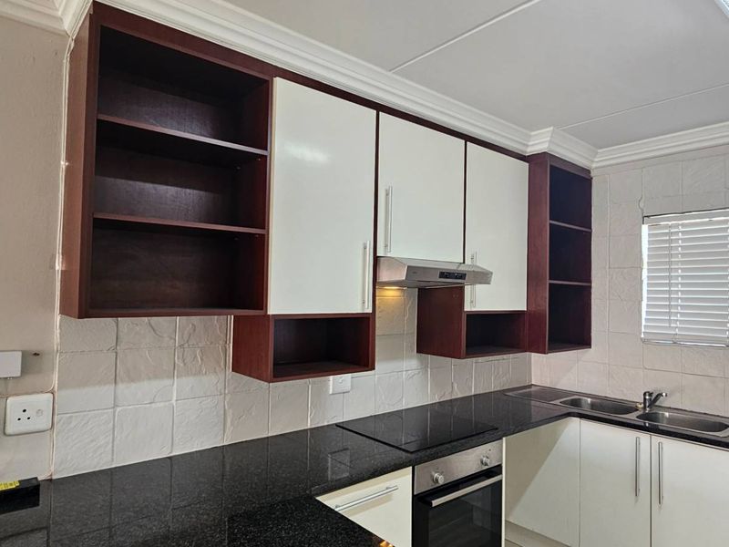 A functional kitchen featuring granite countertops, built-in oven, electric hob, extractor fan, and ample cabinetry with some open shelving.