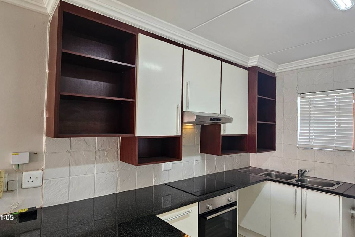 A functional kitchen featuring granite countertops, built-in oven, electric hob, extractor fan, and ample cabinetry with some open shelving.