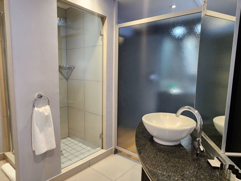 Modern bathroom featuring a glass-enclosed shower, a stylish vessel sink set on a granite vanity, and contemporary tiled finishes.