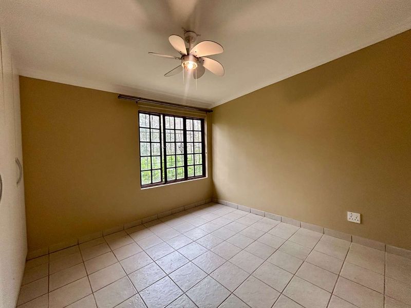 A clean, empty bedroom featuring tiled flooring, a ceiling fan, and built-in cupboards, offering a neutral canvas for personalization.