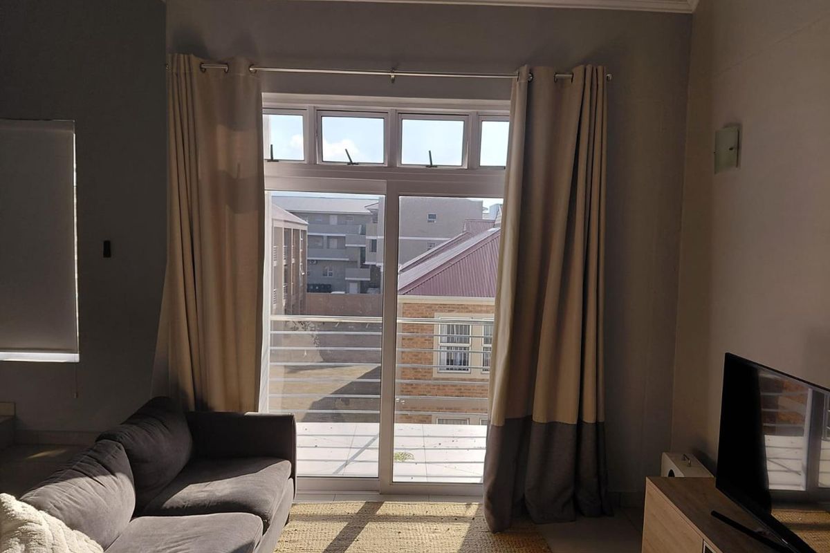 A living room featuring a sliding glass door that opens onto a balcony with metal railings, providing natural light and an urban view.