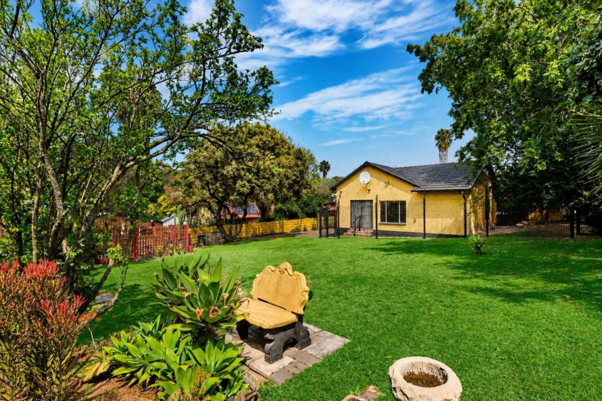 A view of the rear exterior of the house featuring a yellow brick facade, tiled roof, and a spacious, well-maintained garden.