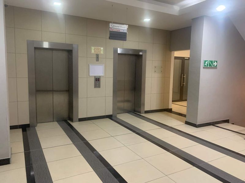 A clean and modern office building lobby featuring dual stainless steel elevators, tiled flooring, and recessed lighting.