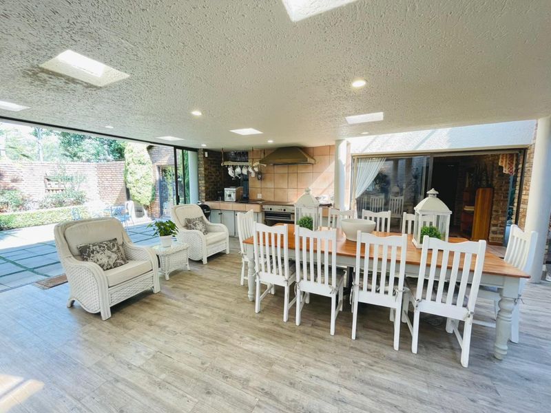 Spacious open-plan living and dining area featuring a built-in kitchen, modern wood-look flooring, multiple skylights, and seamless access to the outdoor patio.