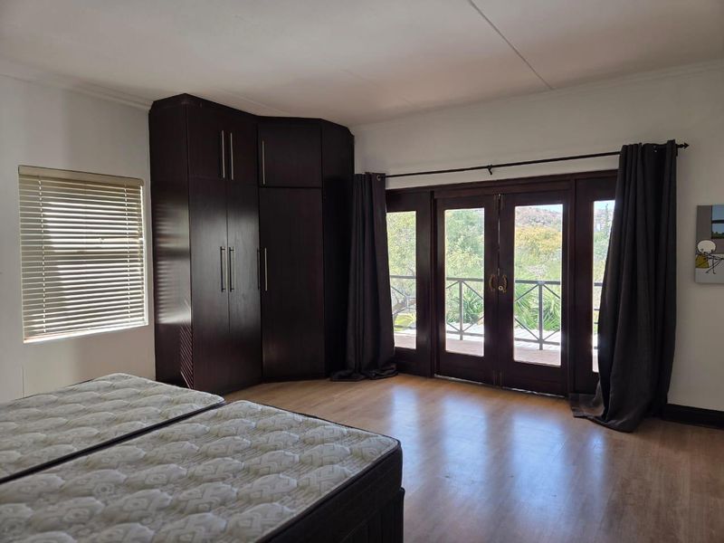 Spacious bedroom featuring dark wood built-in cupboards, laminate flooring, and double french doors opening onto a balcony with natural light.