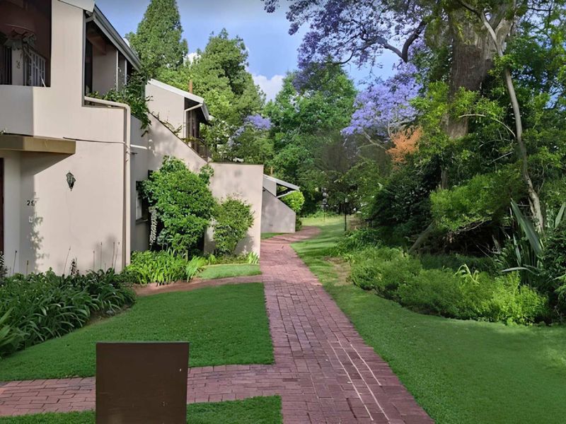 A view of the apartment complex exterior featuring a well-maintained brick pathway, lush green garden, and mature trees.