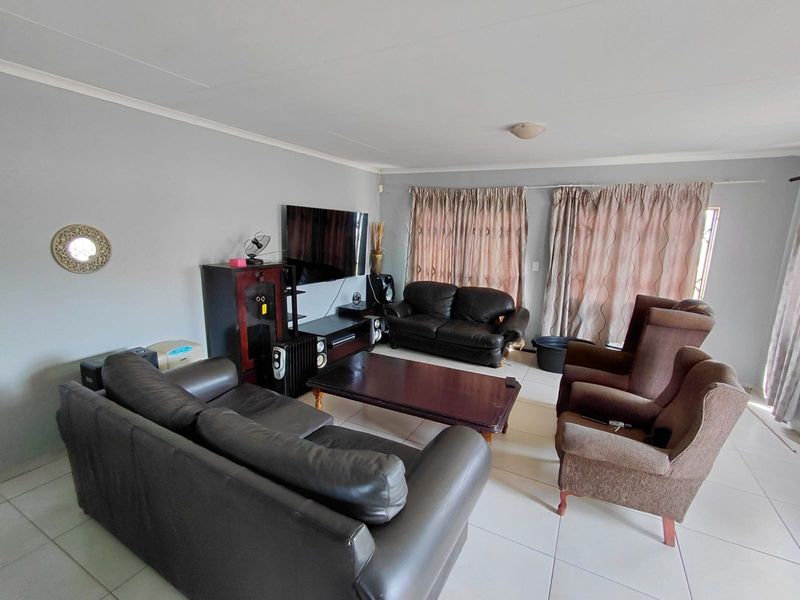 A spacious living room featuring neutral tiled flooring and large windows with curtain rails, offering a functional and well-lit living space.