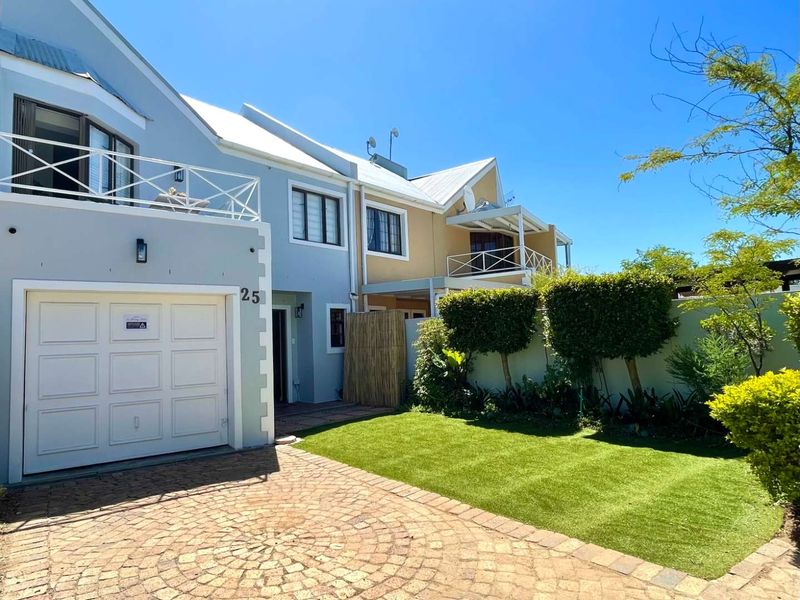 Front exterior view of a townhouse featuring a paved driveway, single garage, manicured lawn, and upper-level balconies with metal roofing.